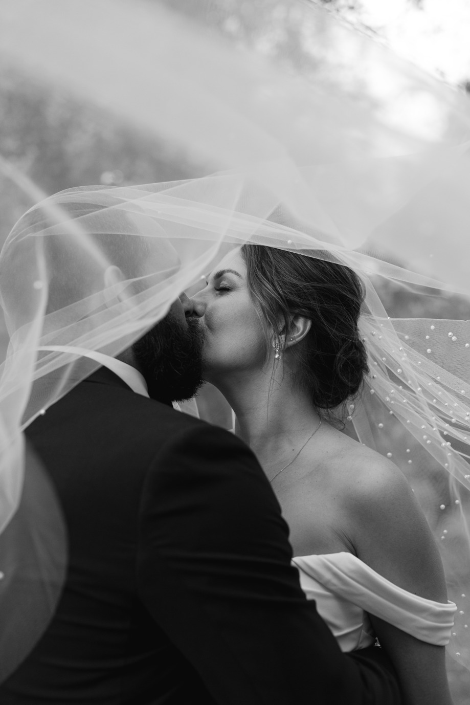 Artistic image of bride and groom kissing with veil blowing over them